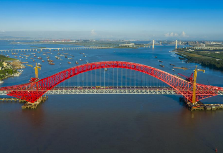 明珠灣大橋位于廣州市南沙區(qū)龍穴南水道之上，是粵港澳大灣區(qū)的重要連接通道。大橋工程全長約10.42公里，主線全長約9.1公里，主橋采用中承式六跨連續(xù)鋼桁拱橋，全長1016米，為同類型橋梁最大跨度。氣勢恢宏的明珠灣大橋綿延伸向遠方，將南沙多條核心主干道緊緊連在一起，構(gòu)筑了明珠灣區(qū)內(nèi)部核心交通環(huán)，是廣州面向粵港澳大灣區(qū)建設(shè)的交通樞紐工程和地標性建筑。圖為南沙明珠灣大橋。